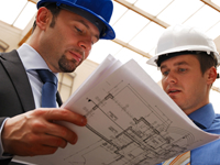 Two men in hard hats looking at a blueprint.